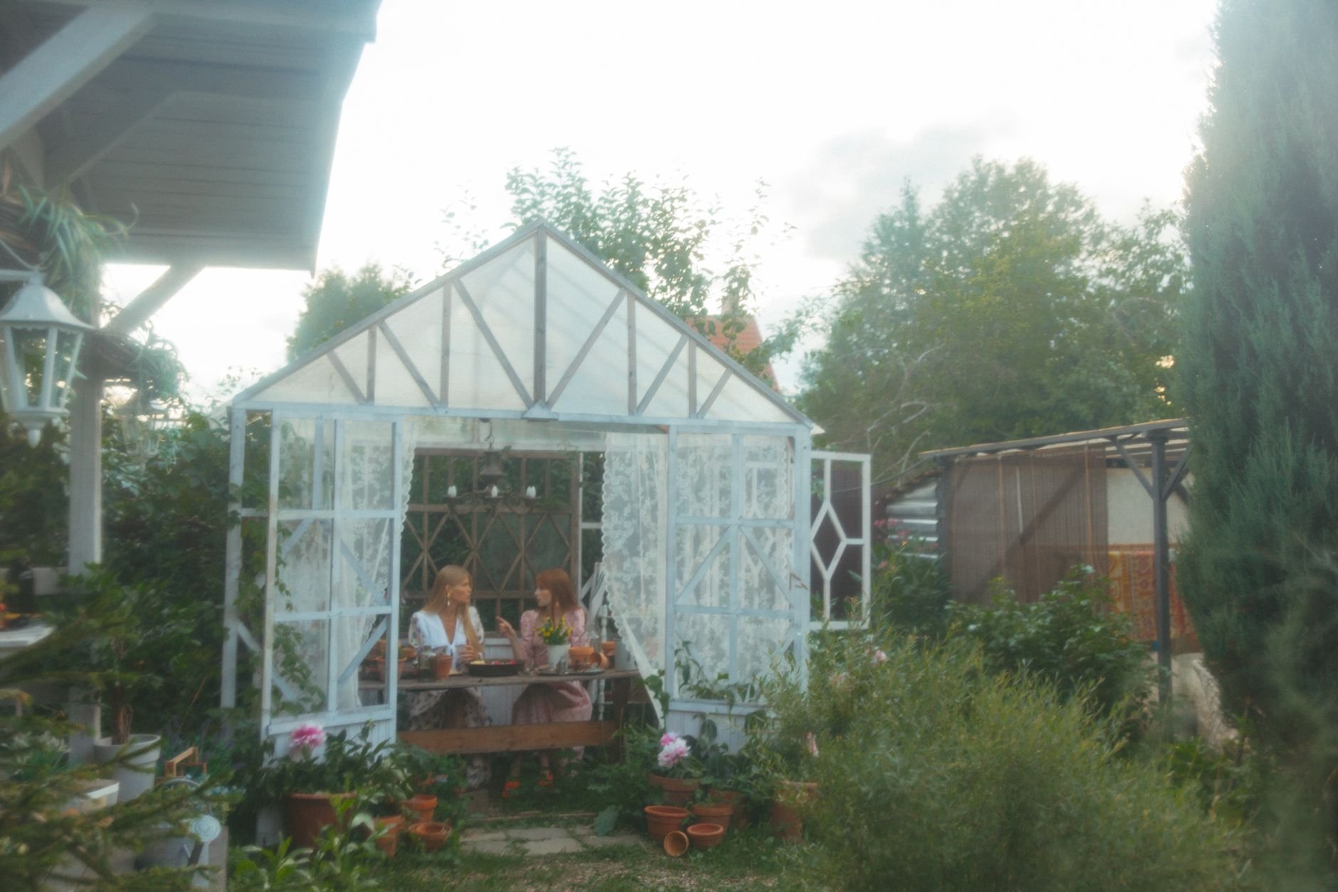 Two women talk quietly together in a warm, plant-filled greenhouse